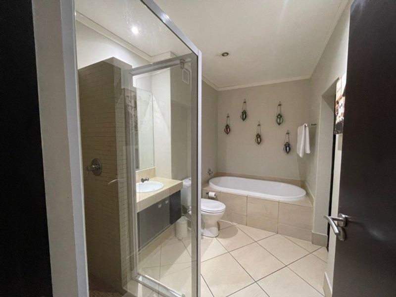 A well-appointed bathroom featuring a glass-enclosed shower, a built-in vanity with basin, a toilet, and a tiled bathtub surround.