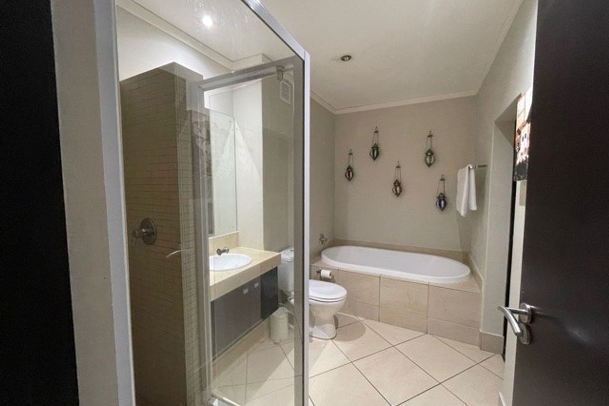 A well-appointed bathroom featuring a glass-enclosed shower, a built-in vanity with basin, a toilet, and a tiled bathtub surround.