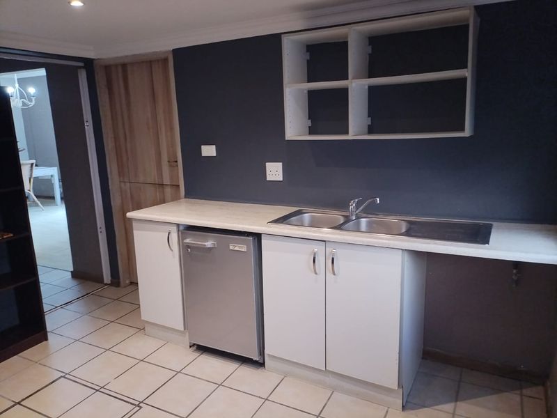 Kitchen area featuring a double bowl sink, laminate countertops, built-in cabinetry, and tiled flooring, with an adjacent room visible through the doorway.
