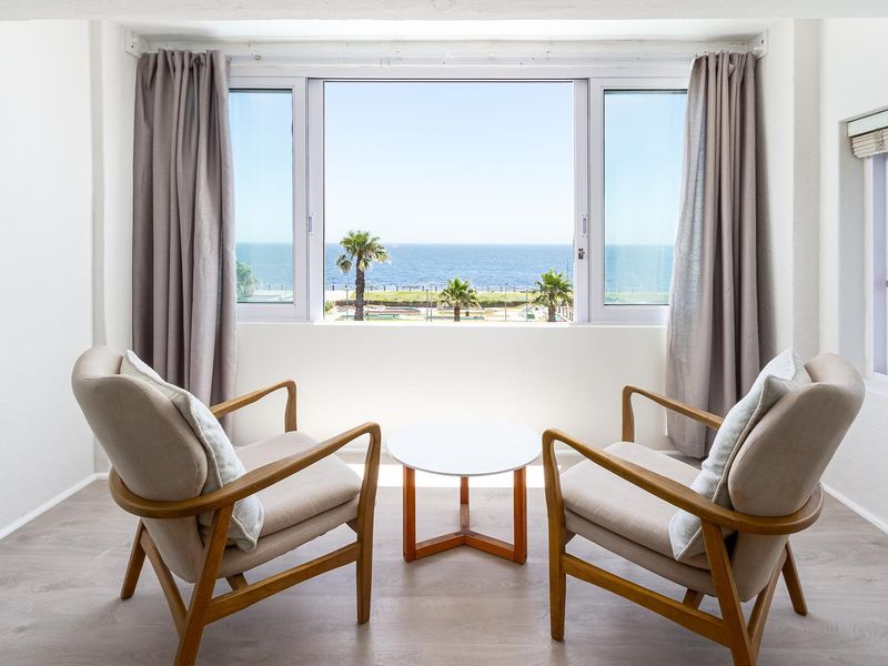 A bright living area featuring large windows that frame a scenic ocean view, complemented by modern laminate flooring.