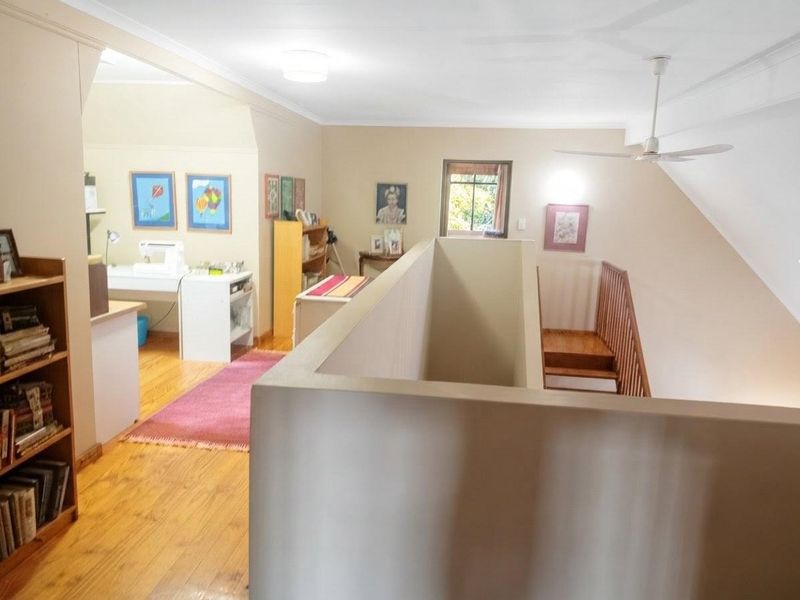 An open landing area featuring timber flooring, a ceiling fan, and a staircase with a timber balustrade overlooking the lower level.