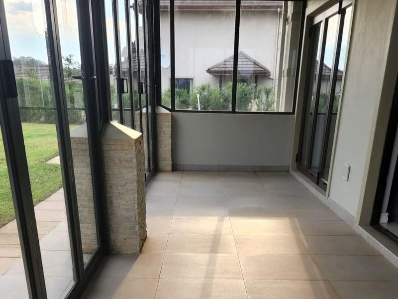 A bright, enclosed patio featuring large stacking glass doors, stone-clad pillars, and neutral tiled flooring, offering a seamless transition to the garden.