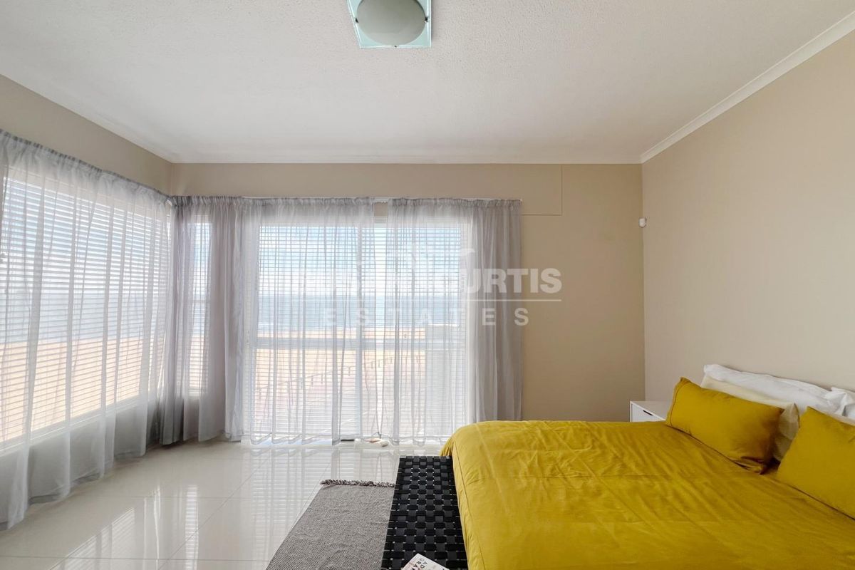 Spacious bedroom featuring large windows with natural light, neutral wall finishes, and tiled flooring, offering a bright and airy atmosphere.