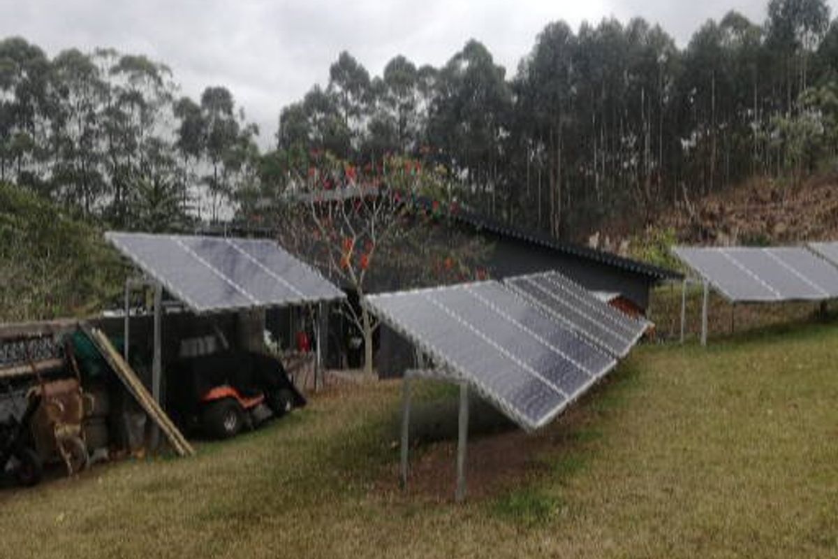 Rear exterior view of the property featuring ground-mounted solar panel arrays and a pitched roof structure set against a wooded backdrop.
