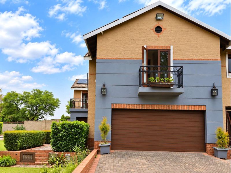 Front elevation of a two-story residential property featuring a double garage, brick paved driveway, and a small upper-level balcony with wrought iron railings.