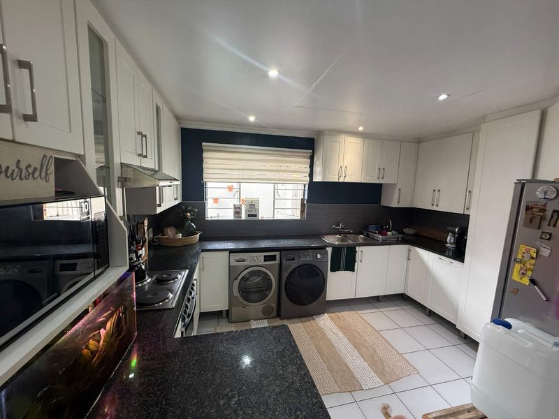 A functional kitchen featuring white cabinetry, dark granite countertops, integrated appliances, and tiled flooring with ample storage space.