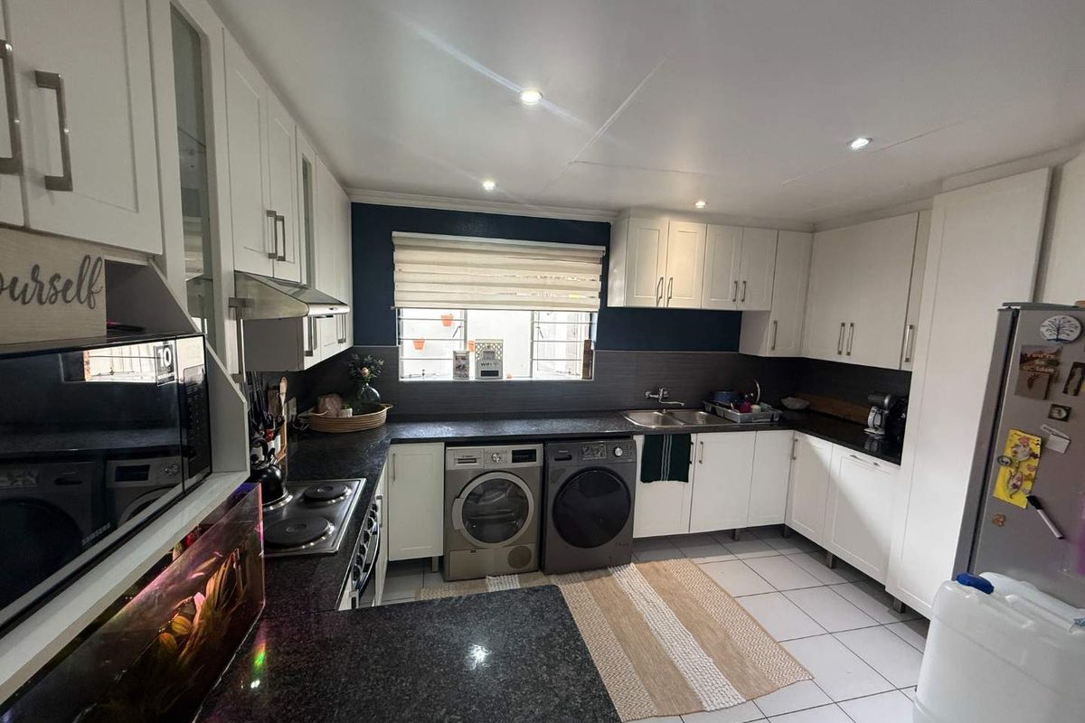 A functional kitchen featuring white cabinetry, dark granite countertops, integrated appliances, and tiled flooring with ample storage space.