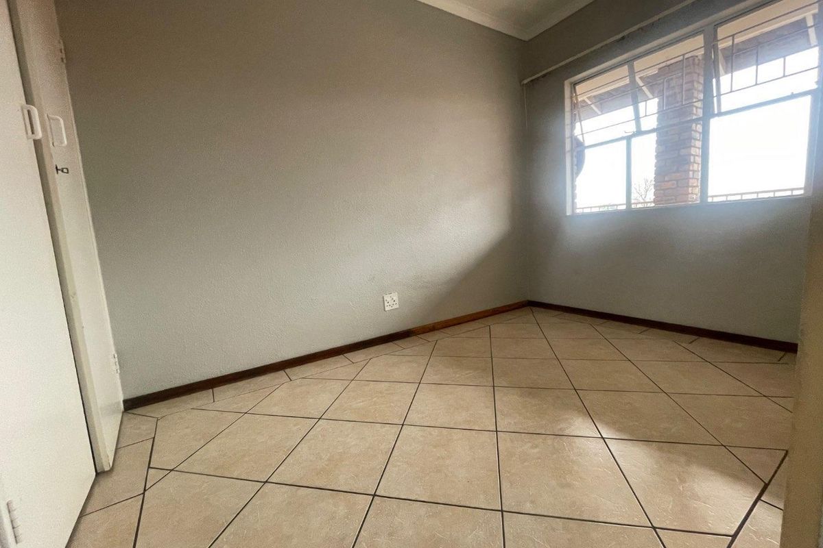 An empty bedroom featuring neutral wall paint, tiled flooring, and a built-in cupboard, offering a clean canvas for personalization.