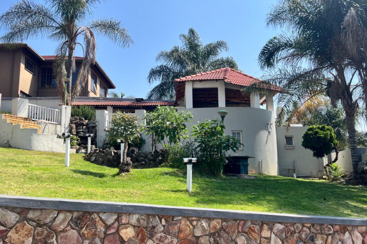 Rear view of the property featuring a landscaped garden, stone retaining wall, and a covered patio area with terracotta roof tiles.