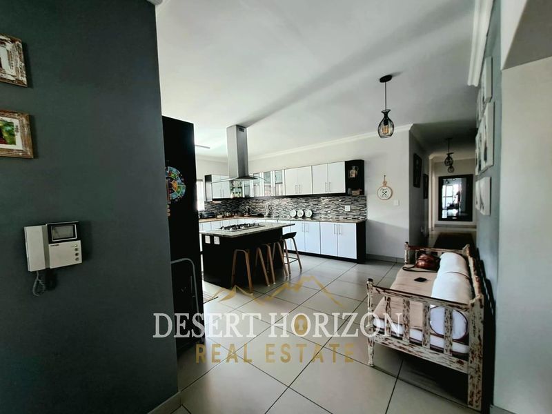 Modern open-plan kitchen featuring a central island with gas hob, sleek cabinetry, and tiled flooring, seamlessly flowing into the living area.