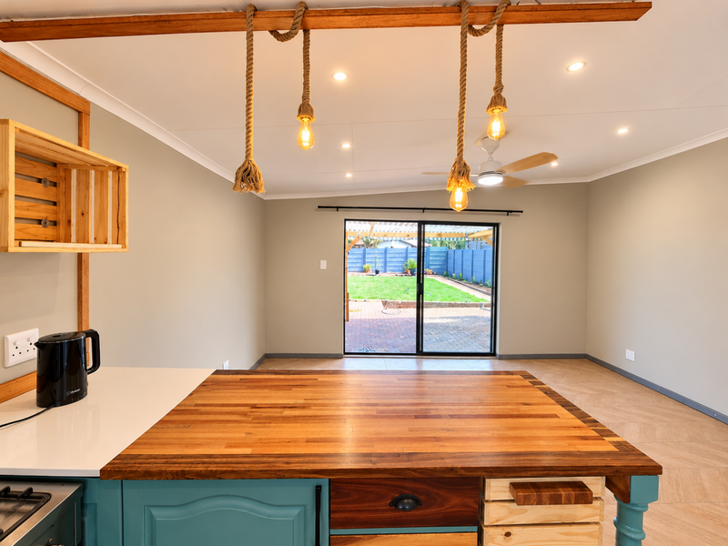 Spacious open-plan living area featuring a custom butcher block island, herringbone flooring, and direct access to the rear patio and garden.