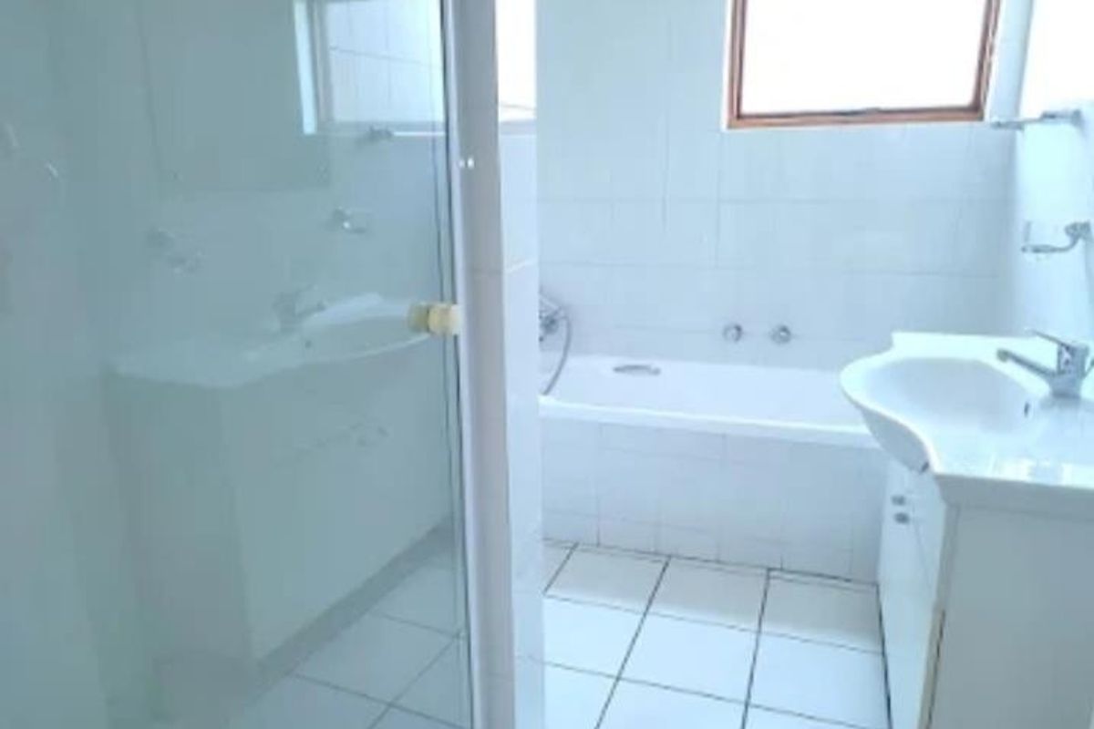 A functional bathroom featuring a white bathtub, a glass-enclosed shower, and a vanity basin with tiled flooring and walls.