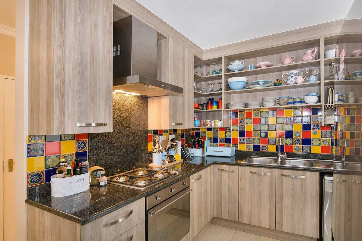 Modern kitchen featuring wood-grain cabinetry, granite countertops, a gas hob with extractor fan, and a vibrant multi-colored tiled backsplash.