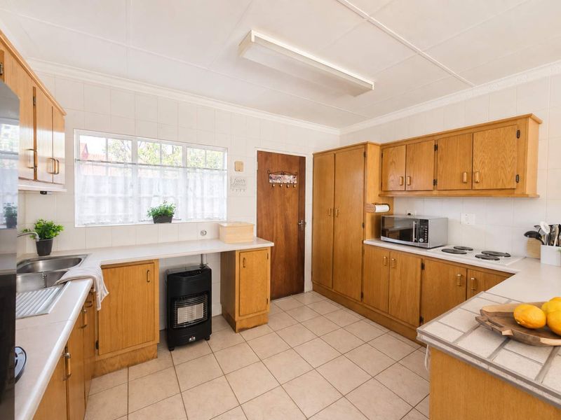 A functional kitchen featuring wooden cabinetry, laminate countertops, a double bowl sink, and an electric hob with tiled splashbacks and flooring.