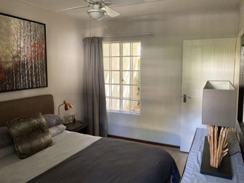 A well-lit bedroom featuring a ceiling fan, grid-pattern window, and neutral wall finishes, providing a comfortable and functional living space.