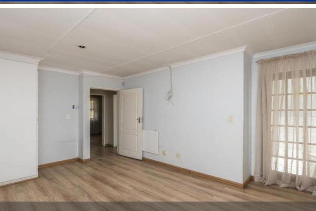 A bright, empty bedroom featuring built-in cupboards, wood-look laminate flooring, and a glass-paneled door providing access to the exterior.
