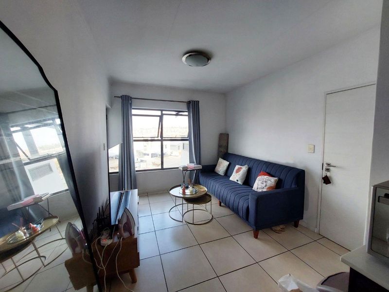 A compact living room featuring tiled flooring, a large window with natural light, and a neutral interior finish.