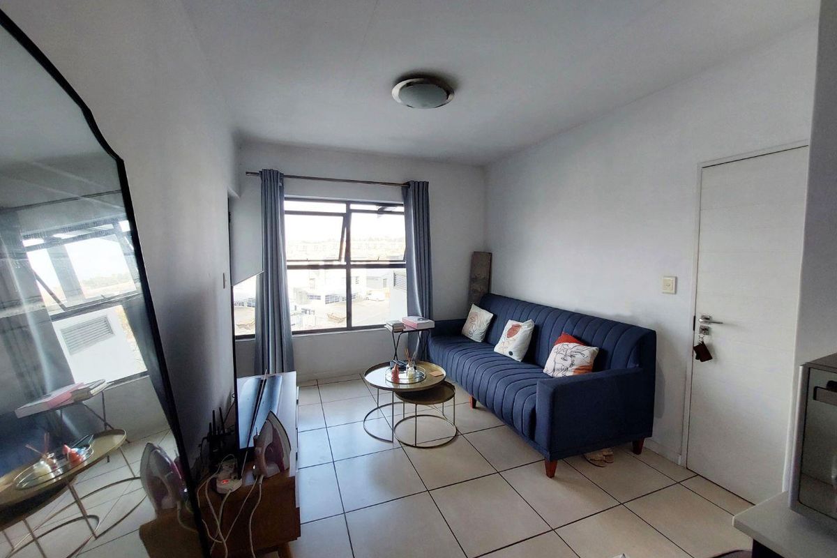 A compact living room featuring tiled flooring, a large window with natural light, and a neutral interior finish.