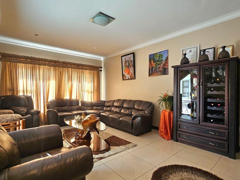 A spacious living room featuring neutral tiled flooring, recessed lighting, and large sliding glass doors with floor-to-ceiling curtains.