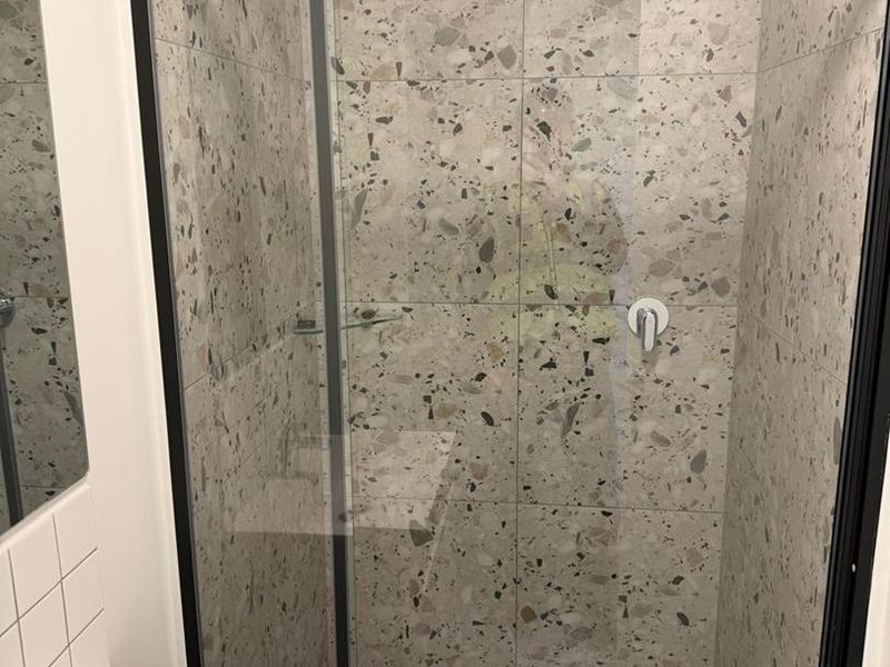 Modern bathroom featuring a walk-in shower with black-framed glass screen and stylish terrazzo-style tiling throughout.