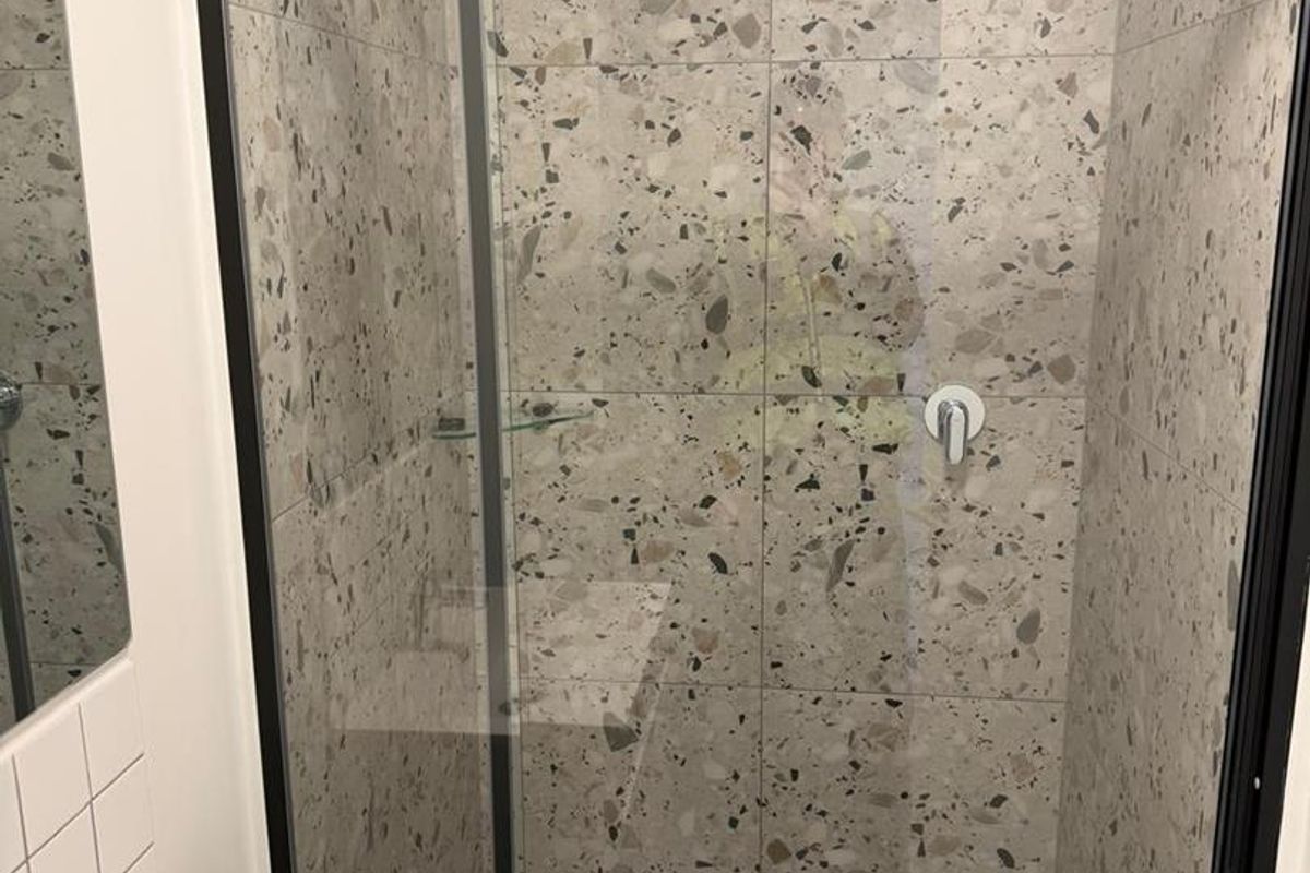 Modern bathroom featuring a walk-in shower with black-framed glass screen and stylish terrazzo-style tiling throughout.