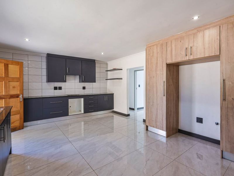 Modern kitchen featuring dark cabinetry, light wood-look pantry storage, tiled flooring, and a tiled backsplash with recessed downlighting.