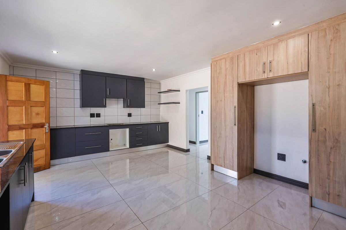 Modern kitchen featuring dark cabinetry, light wood-look pantry storage, tiled flooring, and a tiled backsplash with recessed downlighting.