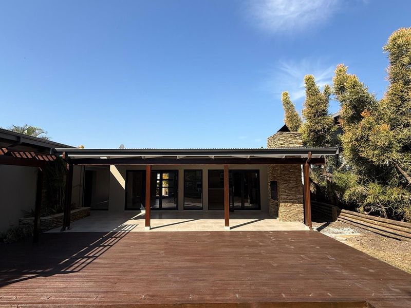 Spacious covered patio featuring timber decking, a stone-clad outdoor fireplace, and large sliding glass doors providing seamless indoor-outdoor flow.