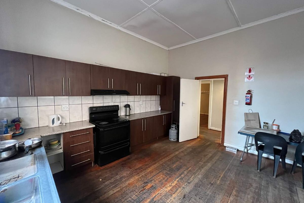 A functional kitchen featuring dark wood cabinetry, a built-in stove with extractor fan, tiled backsplash, and original timber flooring.
