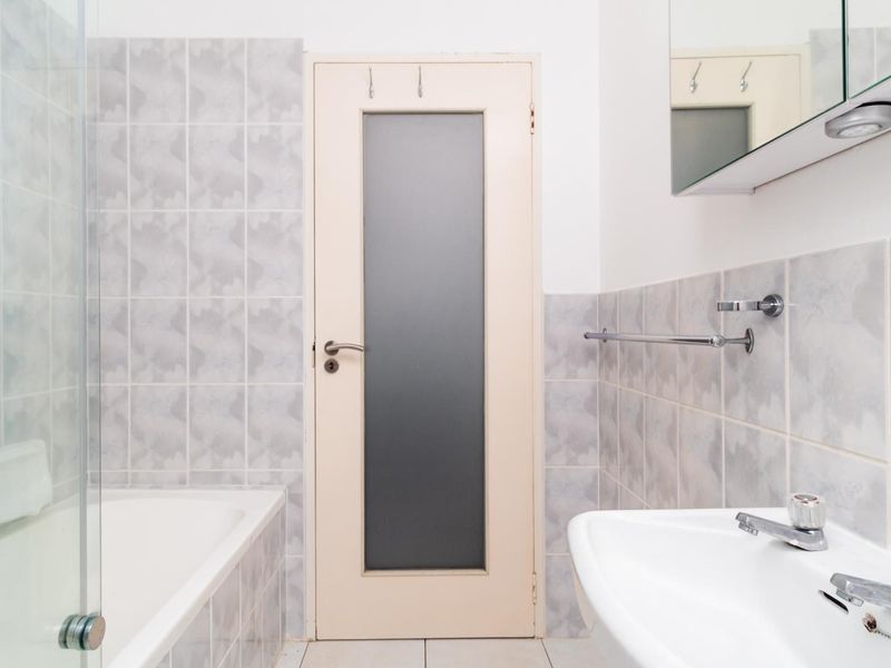 A functional bathroom featuring a bathtub with a glass screen, pedestal basin, and tiled walls, offering a clean and practical layout.
