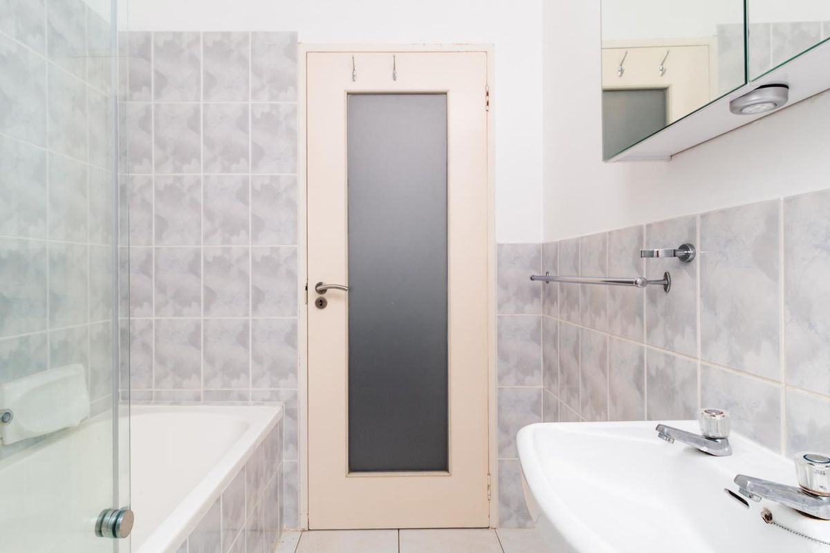 A functional bathroom featuring a bathtub with a glass screen, pedestal basin, and tiled walls, offering a clean and practical layout.