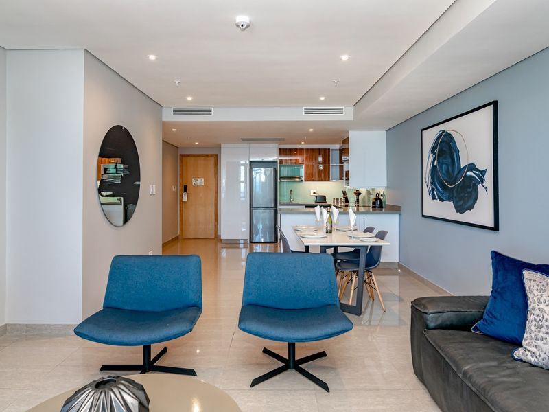 Modern open-plan living and kitchen area featuring sleek cabinetry, stone countertops, integrated appliances, recessed lighting, and polished porcelain floor tiles.