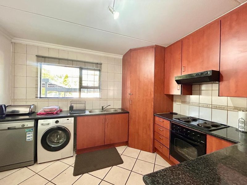 Functional kitchen featuring laminate cabinetry, granite countertops, built-in oven with hob, and tiled finishes, offering a practical layout for daily use.