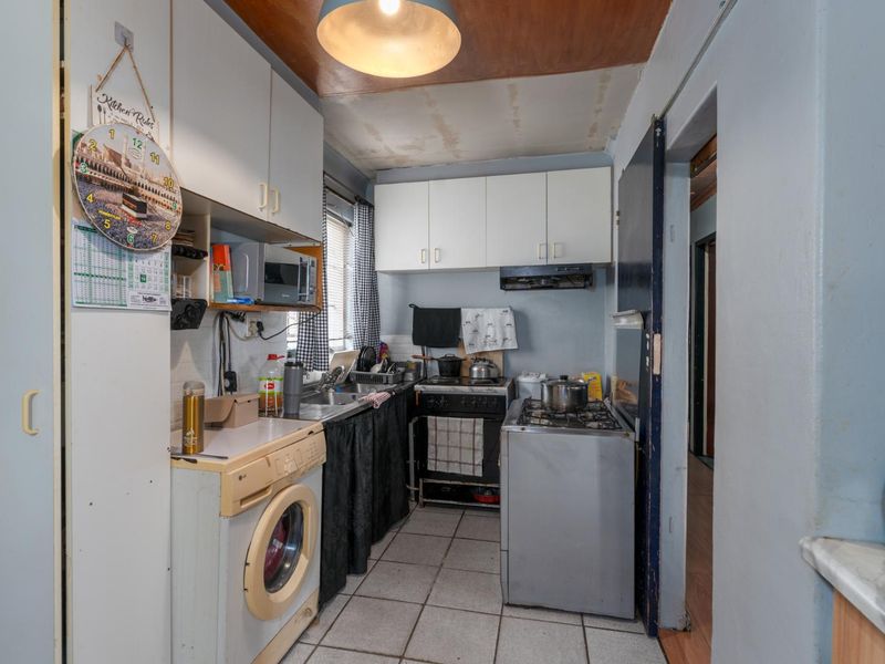 A compact kitchen featuring built-in cabinetry, tiled flooring, and a functional layout with integrated sink and extractor fan, requiring cosmetic updates.