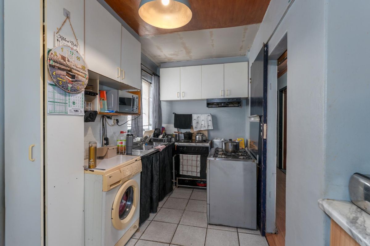 A compact kitchen featuring built-in cabinetry, tiled flooring, and a functional layout with integrated sink and extractor fan, requiring cosmetic updates.