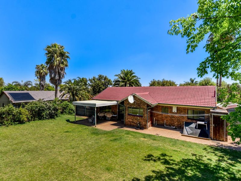 Rear view of a brick house featuring a tiled roof, a covered patio area, and a spacious garden with established trees.