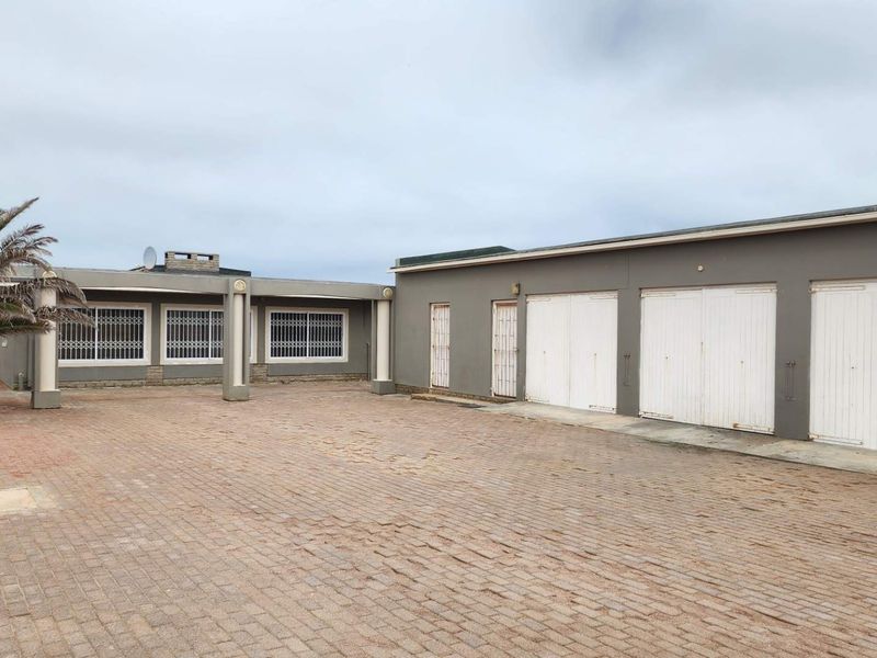 Rear exterior view featuring a large paved courtyard, triple garage with white doors, and a covered patio area with security bars.