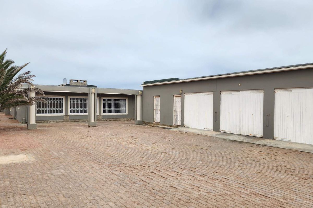 Rear exterior view featuring a large paved courtyard, triple garage with white doors, and a covered patio area with security bars.