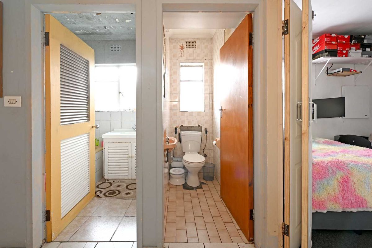 A view into a dated bathroom and separate toilet area, featuring original tiling and fixtures, accessible from an adjacent bedroom.