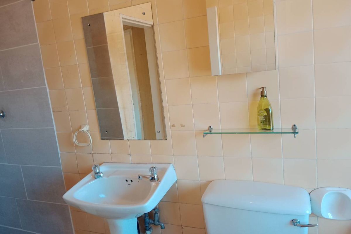 A functional bathroom featuring a pedestal basin, toilet, and shower enclosure with dated wall tiling and wall-mounted fixtures.