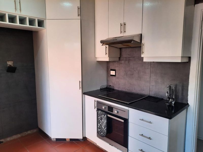 Modern kitchen featuring white cabinetry, dark stone countertops, integrated oven, electric hob, and extractor fan with a contemporary tiled splashback.