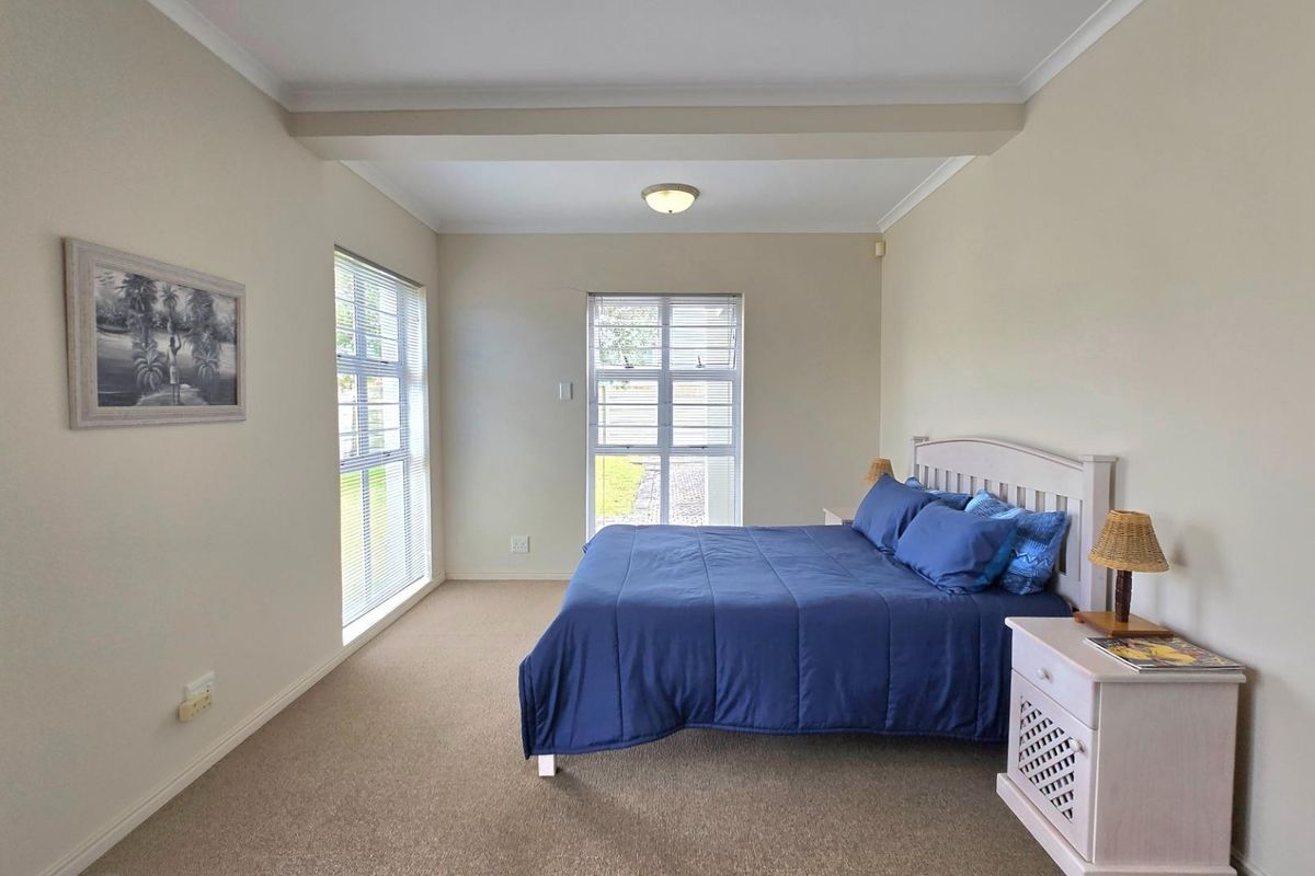 A spacious bedroom featuring neutral wall tones, carpeted flooring, and large windows with fitted blinds, providing ample natural light.