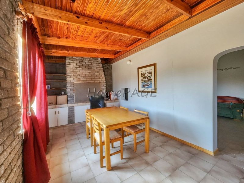 Living area featuring a rustic exposed timber beam ceiling, brick fireplace, and tiled flooring, with an arched entryway leading to adjacent space.
