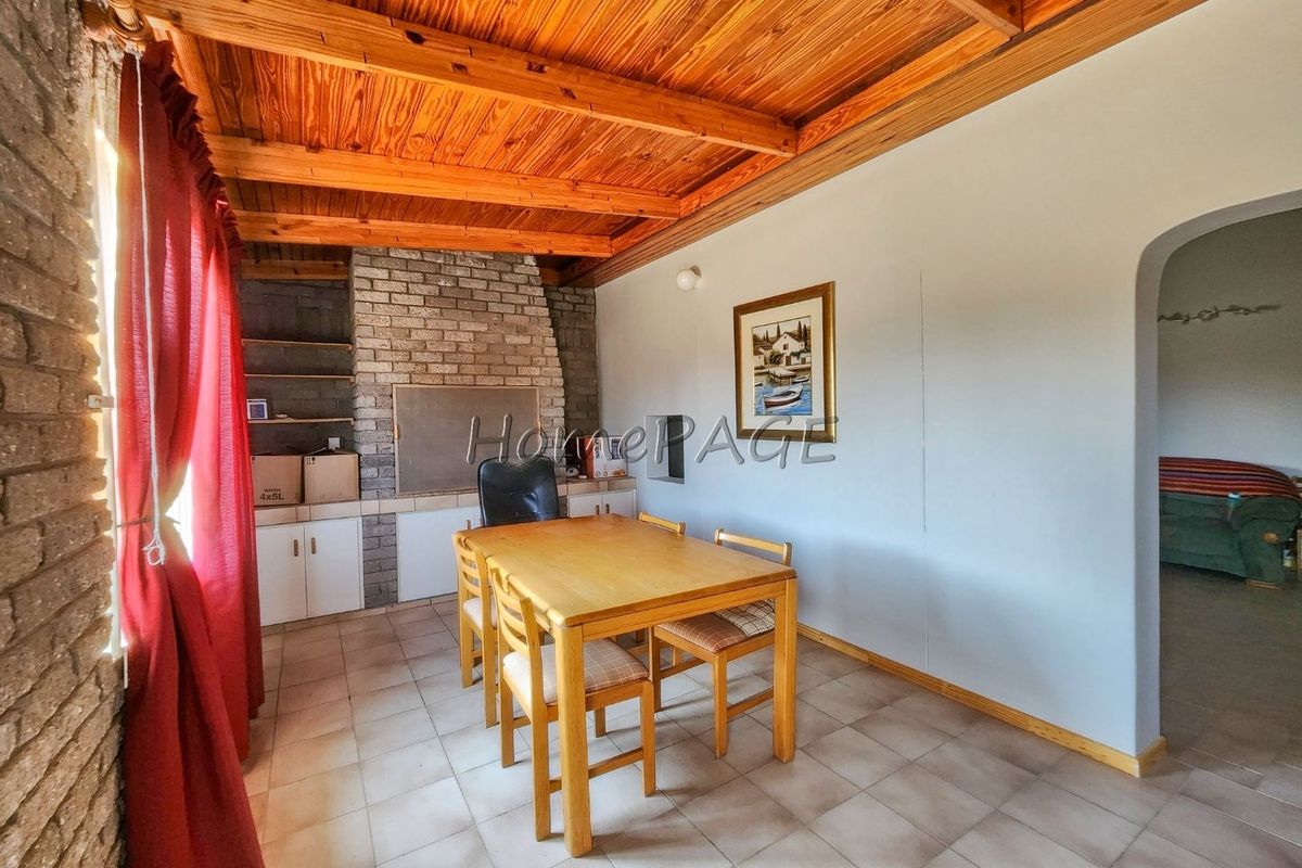 Living area featuring a rustic exposed timber beam ceiling, brick fireplace, and tiled flooring, with an arched entryway leading to adjacent space.