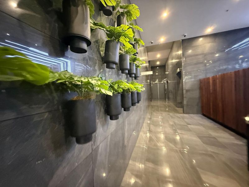 A modern office hallway featuring polished stone wall and floor tiles, recessed ceiling lighting, and integrated wall-mounted decorative planters.