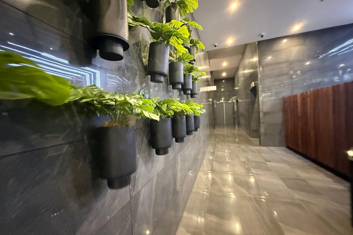 A modern office hallway featuring polished stone wall and floor tiles, recessed ceiling lighting, and integrated wall-mounted decorative planters.