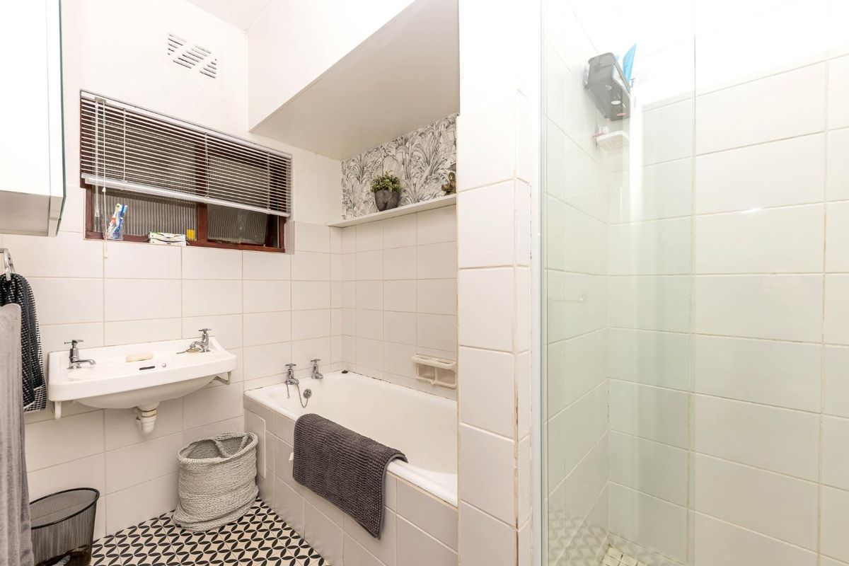 A functional bathroom featuring a built-in bathtub, separate glass-enclosed shower, wall-mounted basin, and patterned floor tiling.