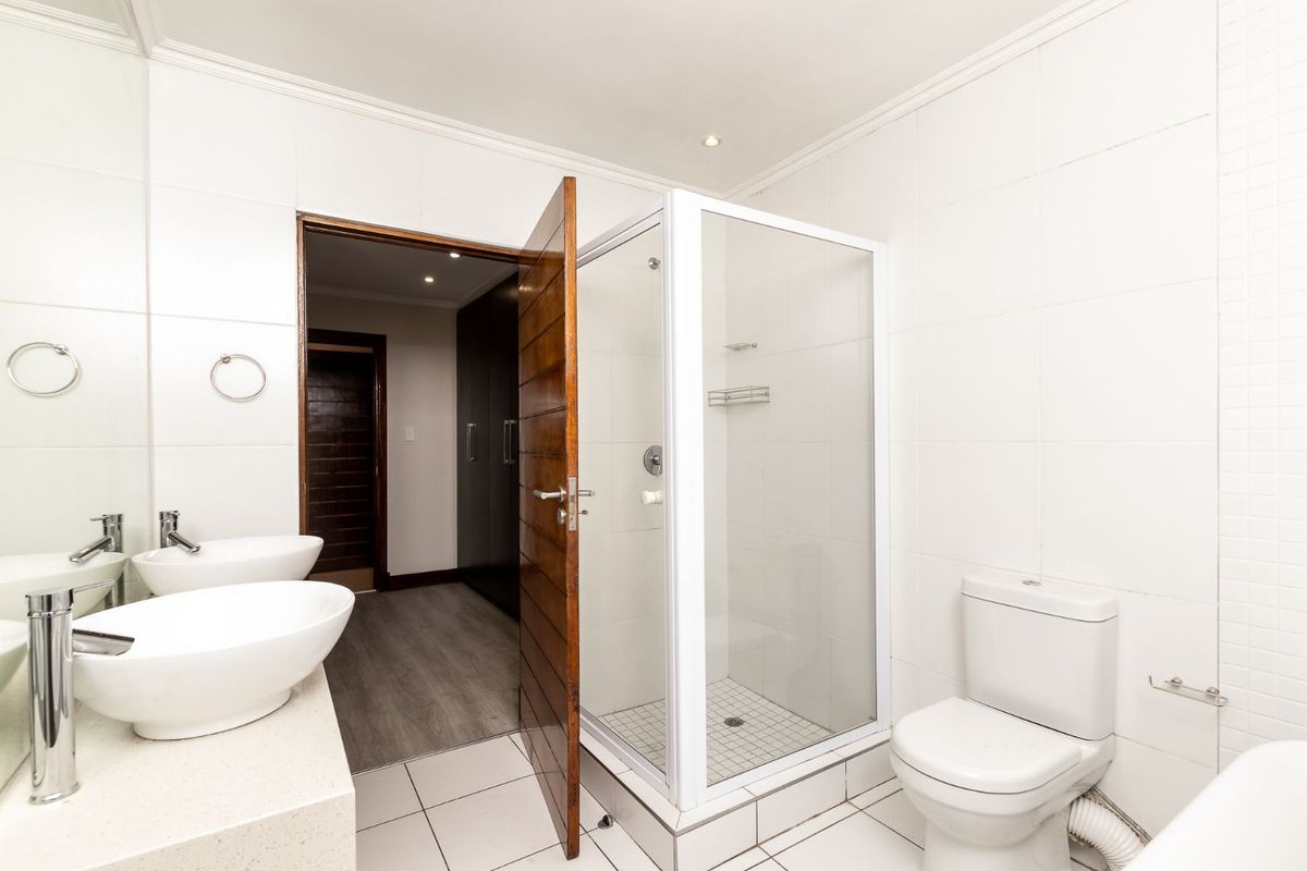 A clean, modern bathroom featuring a glass shower enclosure, dual vessel sinks on a stone vanity, and neutral tiled finishes.