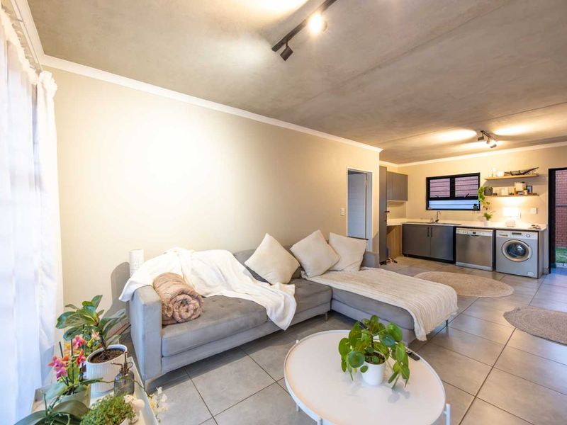 Open-plan living area featuring tiled flooring, track lighting, and a functional kitchen space with integrated laundry plumbing and cabinetry.
