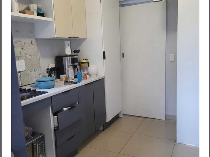 A compact kitchen featuring two-tone cabinetry, a gas hob, and tiled flooring, currently requiring minor repairs to the wall finish and cabinetry.